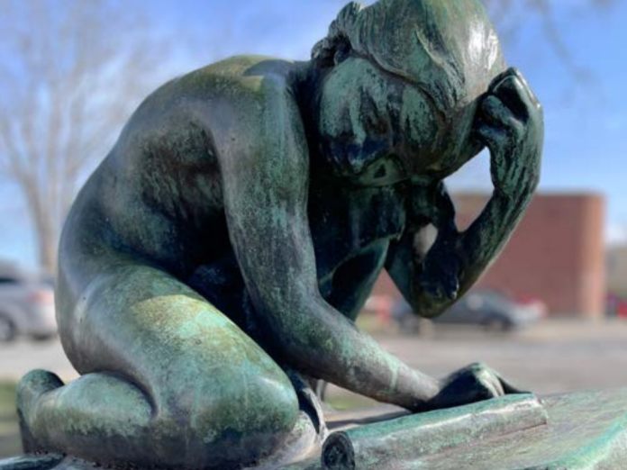 En bronzestatue der viser en pige der sidder foroverbøjet. Titlen på værket er 'Den granskende pige'